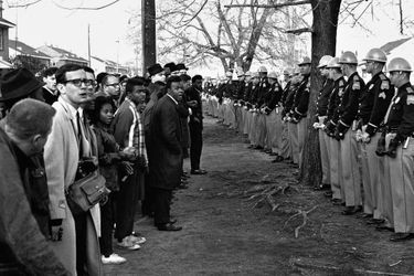 Le 13 mars 1965, à Selma,  des manifestants pour les droits civiques font face à la police. Par AFP. "Le travail n'est pas terminé": Barack Obama célèbre samedi à Selma (Alabama) la marche pour les droits civiques qui a marqué un tournant dans l'histoire des Etats-Unis en garantissant le droit de vote aux Afro-Américains des Etats du Sud.Le premier président noir de l'histoire des Etats-Unis doit s'exprimer devant le pont Edmund Pettus sur lequel, le 7 mars 1965, plusieurs centaines de manifestants pacifiques furent violemment repoussés par la police dans un assaut qui traumatisa l'Amérique et aboutit, quelques mois plus tard, au Voting Rights Act.Barack Obama avait trois ans au moment des faits. Il a appris cette histoire par sa mère, quand il avait "six, sept, huit ans". "Elle me donnait des tas de livres pour enfants sur la lutte pour les droits civiques. Elle mettait des chansons de Mahalia Jackson (qui fut une proche de Martin Luther King, NDLR)", a-t-il raconté à la veille de cette célébration.Le discours présidentiel intervient trois jours après la publication d'un rapport accablant du ministère de la Justice pointant les comportements discriminatoires de la police de Ferguson (Missouri), théâtre de violentes émeutes après la mort en août dernier d'un jeune Noir abattu par un policier blanc.Selma, ville de 20.000 habitants (dont 80% de Noirs), se prépare depuis plusieurs jours à ce week-end de commémoration auquel l'ancien président George W. Bush et plus d'une centaine d'élus du Congrès doivent participer.Le 15e amendement de la Constitution américaine, adopté en 1870, interdit de refuser le droit de vote à tout citoyen "sur la base de sa race ou de sa couleur". Dans plusieurs Etats du Sud, il a longtemps été bafoué."Au rythme actuel, il faudra 103 ans pour que les 15.000 Noirs du comté de Dallas puissent s"inscrire sur les listes électorales", lançait Martin Luther King en janvier 1965 à Selma.Si la loi signée le 6 août 1965 par le président Lyndon Johnson a marqué une rupture, nombre d'activistes considèrent que ce chapitre n'est pas clos.