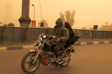 Man and a woman ride on a motorcycle over a bridge during a sand storm in Cairo