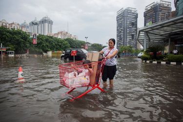 Mother uses a shopping cart to transport her child and groceries through a flooded parking lot at a mall in Kelapa Gading, North Jakarta