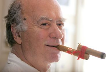 Georges WOLINSKI chez lui à PARIS tente de fumer un cigare bien endommagé.