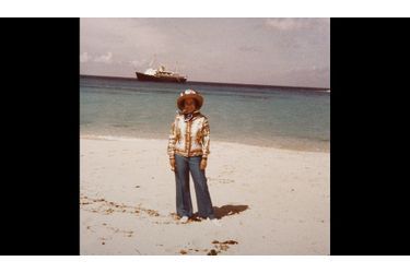 Elizabeth, sur une plage tropicale, avec son yacht adoré, le Britannia, au large - photo non datée, années 1970.