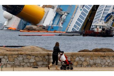 Une femme promène son enfant à proximité du navire échoué Costa Concordia sur l’île du Giglio. Le mauvais temps a retardé les opérations de pompage des cuves du bateau de croisière, qui contiennent 2300 tonnes de carburant.