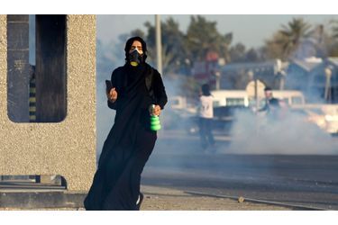 Une femme, équipée d'un téléphone portable, d'un diffuseur et masque à gaz, fuit les gaz lancés par les forces de l'ordre lors d'une manifestation à Diah, au Bahreïn.