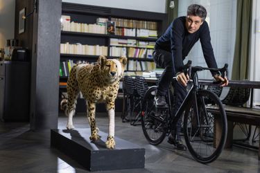 Chez lui, à Paris, sur un vélo fabriqué par sa société Heroïn. A sa droite, un des « Accidents de chasse » du plasticien Pascal Bernier, pour alerter sur la fragilité de l’environnement