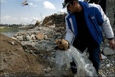Daoud ramasse les restes d’un combattant de Daech dans les décombres. Au fond, le drapeau irakien planté après la bataille. 