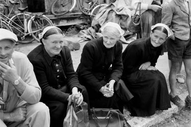 <br />
Le tour de France cycliste de 1954. A la Roche Bernard, des femmes en coiffes bretonnes et robes noires assises sur le bord de la route, sont venues regarder les coureurs cyclistes. 