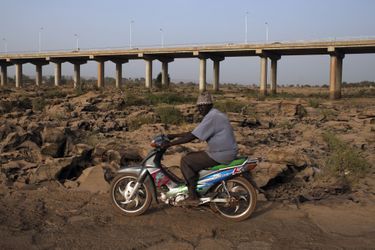 26 février, un homme conduit une moto sur le lit asséché d&#039;une rivière, sous un pont de Bamako. 