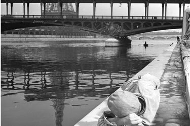 Un homme allongé sur les quais du pont de Bir - Hakeim regardant passer le métro aérien et la Tour Eiffel en arrière-plan 