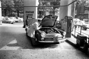Avant l&#039;ouverture du 46e Salon de l&#039;automobile, en septembre 1959, Charles Aznavour vérifie le moteur de son Alfa Romeo 2000 Spider.