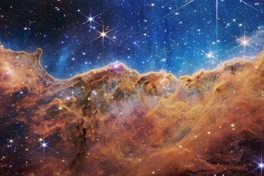 Les &quot;falaises cosmiques&quot; d&#039;une pouponnière d&#039;étoiles dans la nébuleuse de la Carène photographiées par le télescope James-Webb. En orange, du gaz et de la poussière qui vont donner des étoiles.  