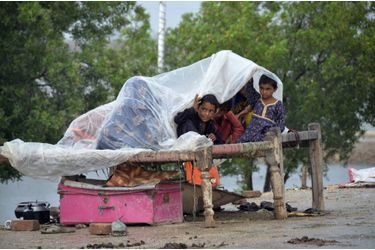 Des enfants se protègent de la pluie sous une bâche de plastique. 