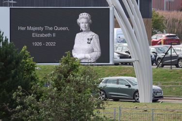 Le cortège royal passe devant un immense portrait de la reine Elizabeth II.