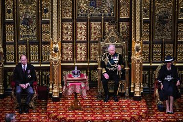 Westminster, 10 May at 11:30. Assistant to the Throne of the Prince Consort, Charles s'apprête à lire le discours écrit par le Prime Minister. Derrière la couronne impériale d'État, le trône de la Reine n'a pas été installé.