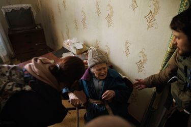 Volunteers Philip and Masha try to convince an elderly lady to follow them.  Because of a bombardment, it no longer has glass in its windows.