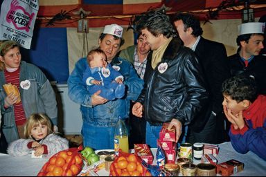 Sous le chapiteau de Gennevilliers, le 22 décembre 1985, Coluche accueille le premier bébé – déjà badgé – sous le regard attendri de Daniel Guichard