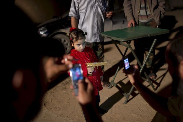 Les habitants de Misrata défilent pour voir le cadavre du tyran et posent avec l’arme. Dans les mains d’une fillette, elle ressemble à un jouet morbide.