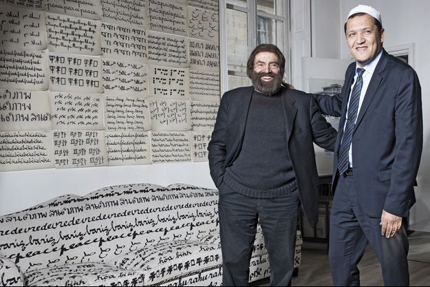 Marek Halter, chez lui devant le mur tapissé du mot "paix", avec Hassen Chalghoumi. 