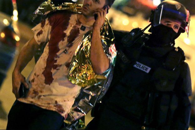 Un homme, le tee-shirt en sang, est accompagné par un policiers aux abords du Bataclan vendredi soir