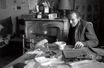 Louis-Ferdinand Céline en 1957 dans sa maison de Meudon. L’écrivain, alors âgé de 63 ans, est assis devant un bol de café posé sur la table sur laquelle se trouve son perroquet Toto avec un stylo dans le bec.